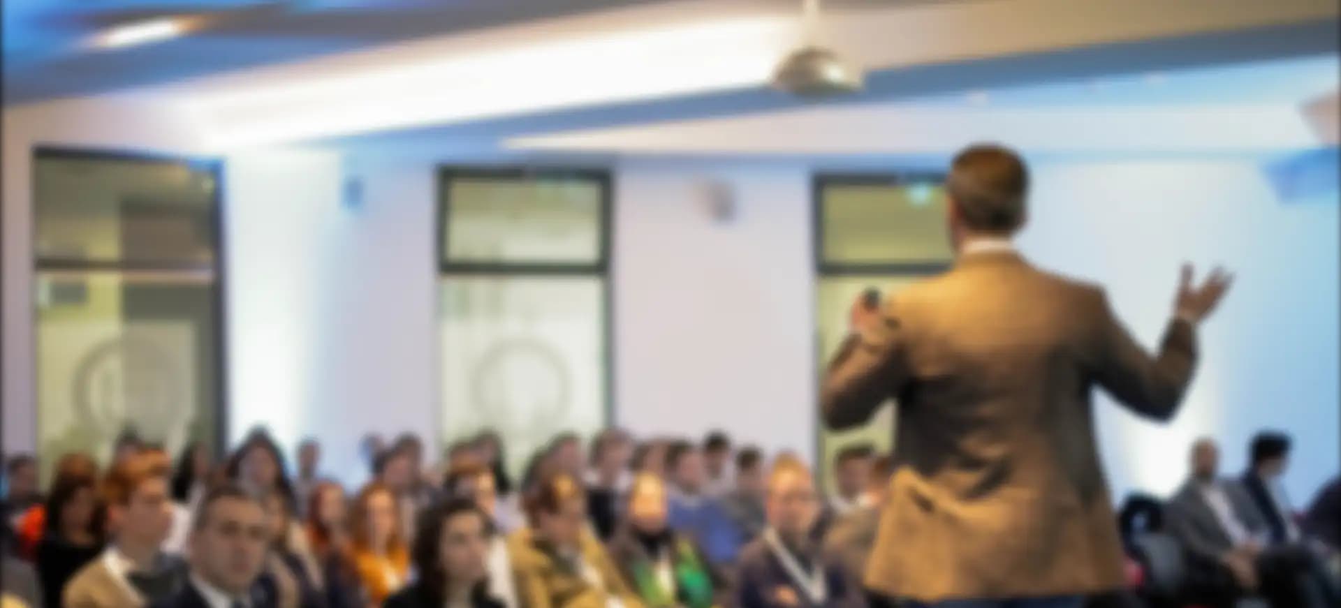 Background image. Blurred image of a person in a suit giving a speech